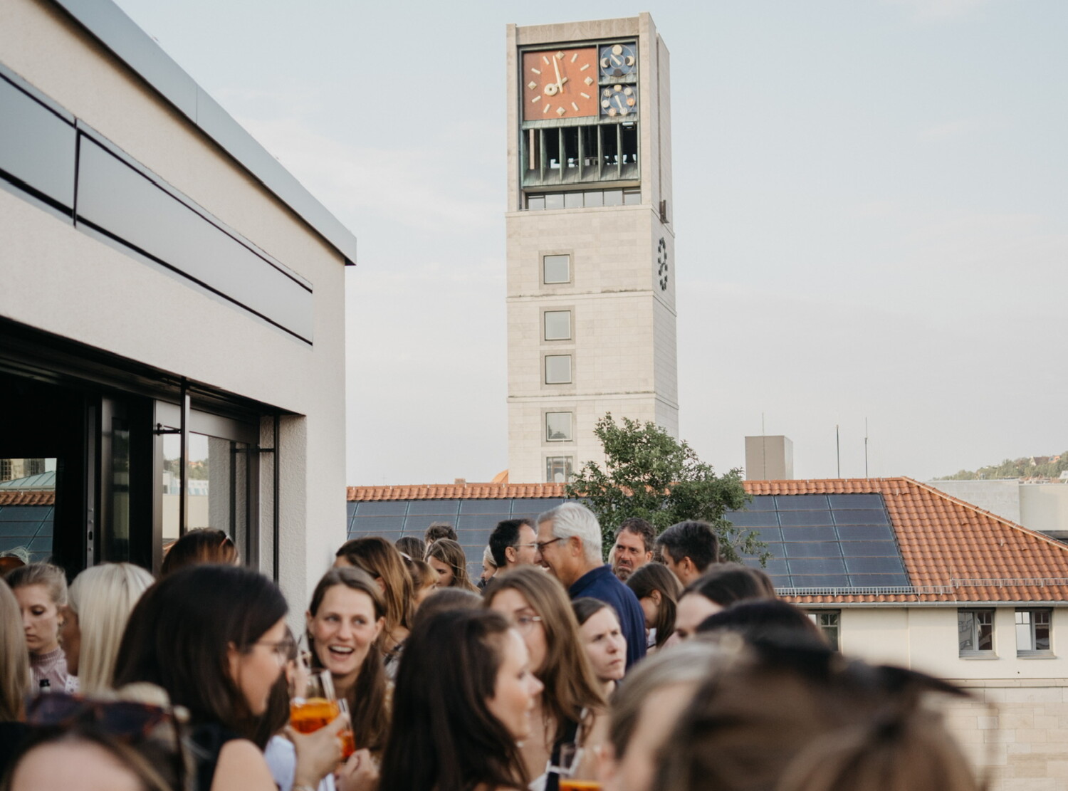Viele Menschen sind auf einer sommerlichen Dachterrasse und genie&szlig;en Drinks