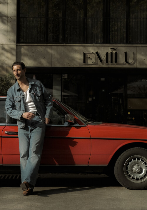 Men in denim clothes leaning on a red car infront of the EmiLu Hotel