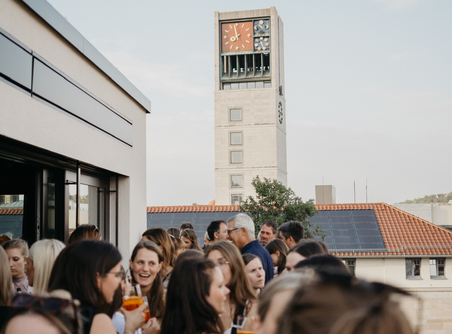 Many people are enjoying drinks on a sunny rooftop terrace, soaking up the summer atmosphere.