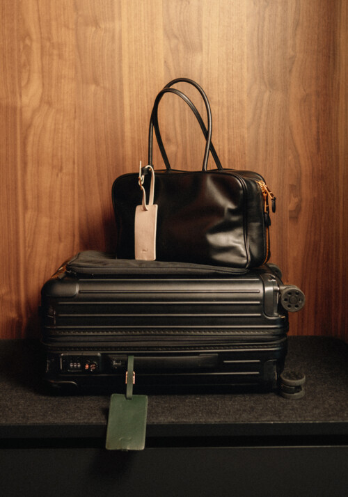 Ein Koffer mit Kofferanh&auml;nger auf welchem eine schwarze Tasche platziert ist