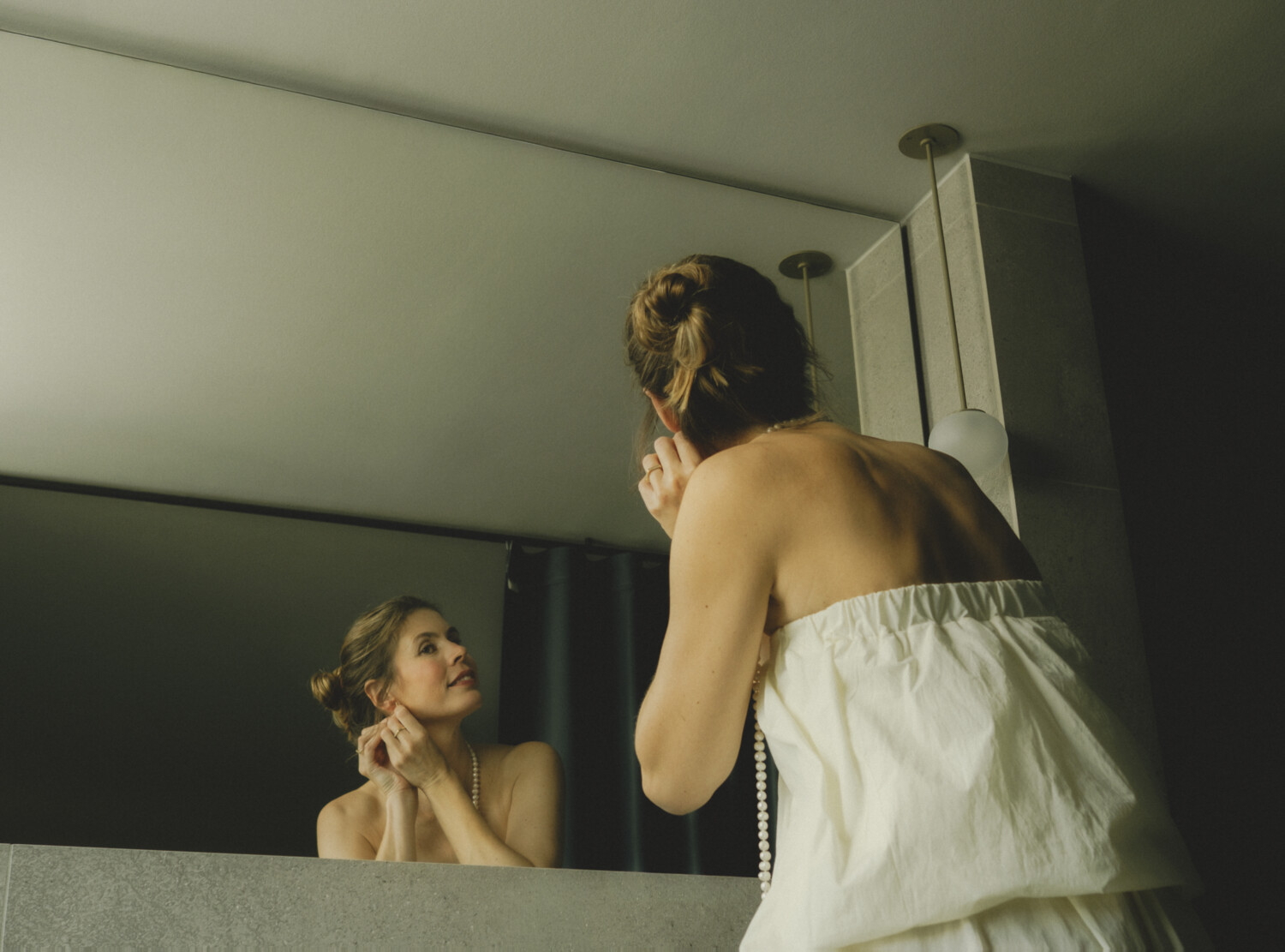 Dame in schickem Kleid zieht sich im Badezimmer die Ohrringe an