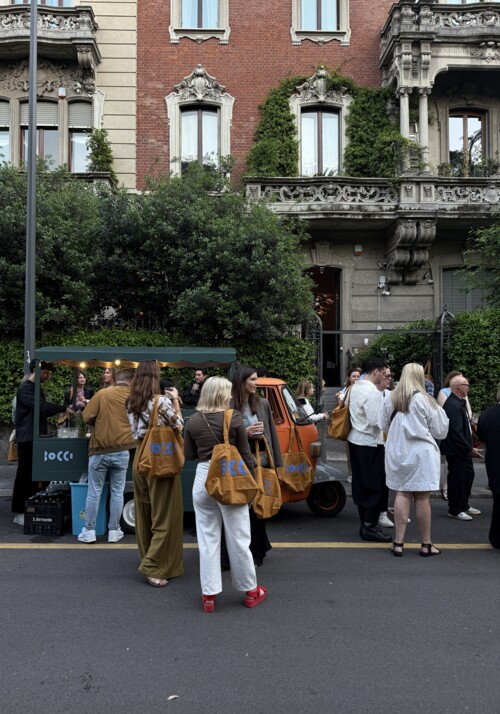 Au&szlig;enaufnahme vor einem Geb&auml;ude mit gr&uuml;ner Bepflanzung und vielen Menschen beim trinken und reden